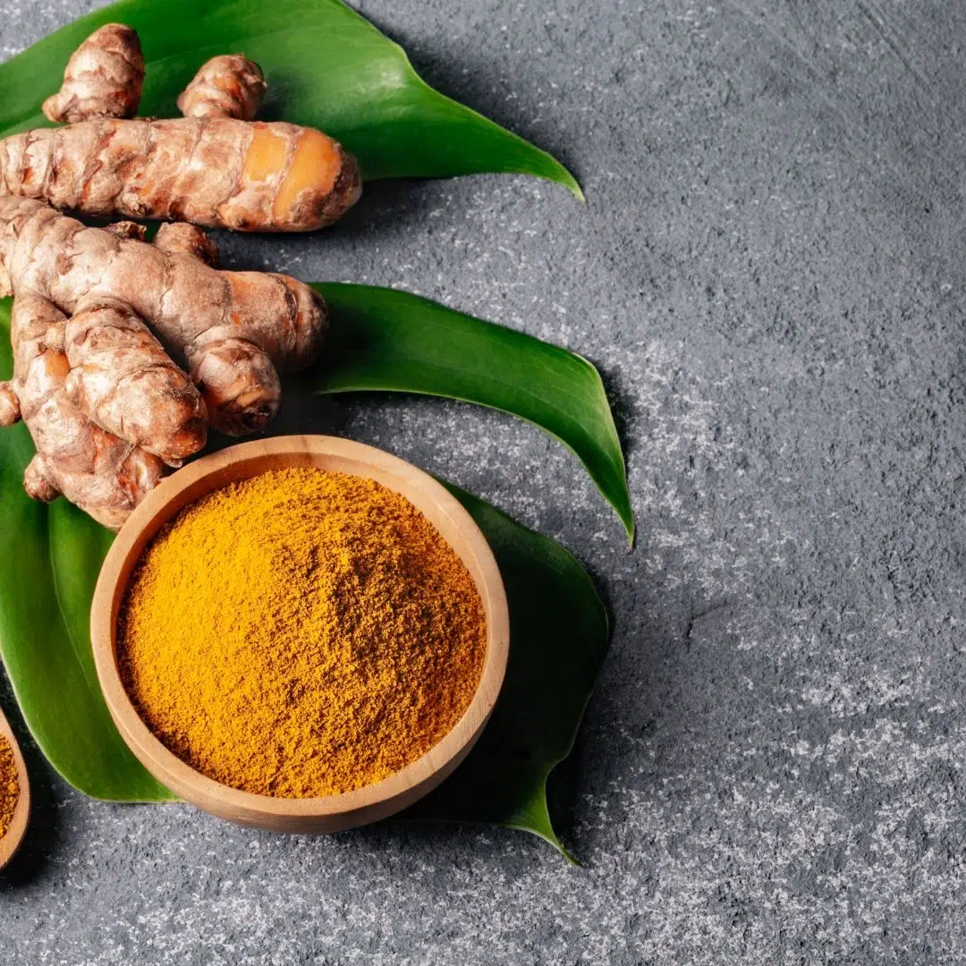 Turmeric root and ground turmeric in a bowl on leaves, representing an anti-inflammatory herb for hormone balance.